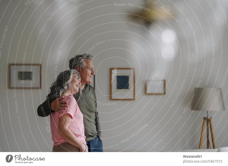 Älteres Ehepaar steht zu Hause im Wohnzimmer Rahmen Bilder Bildnis entspannen relaxen Arm umlegen Umarmung Umarmungen entspanntheit relaxt freuen geniessen