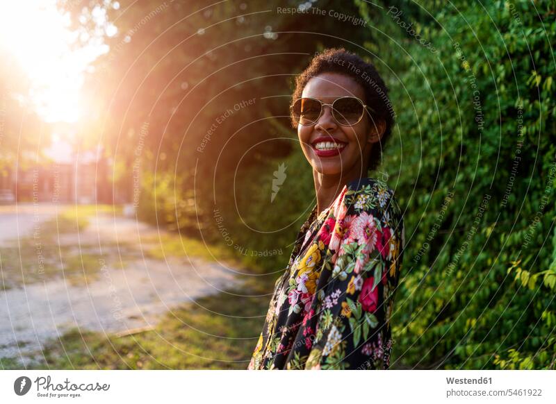 Porträt einer glücklichen jungen Frau mit Sonnenbrille im Freien bei Sonnenuntergang Sonnenbrillen Brille Sonnenuntergänge Portrait Porträts Portraits weiblich