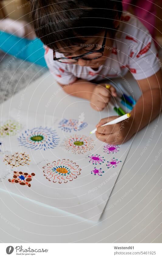 Kleiner Junge liegt zu Hause auf dem Boden und zeichnet Blumen Bilder Bildnis Zeichnungen Kinderzeichnungen Brillen daheim Muße konzentrieren konzentriert