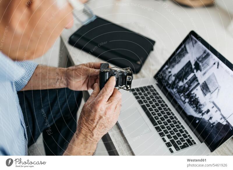 Älterer Mann benutzt Laptop und hält seine alte Fotokamera, Bildschirm mit altem Foto Hobby Hobbies Senior ältere Männer älterer Mann Senioren