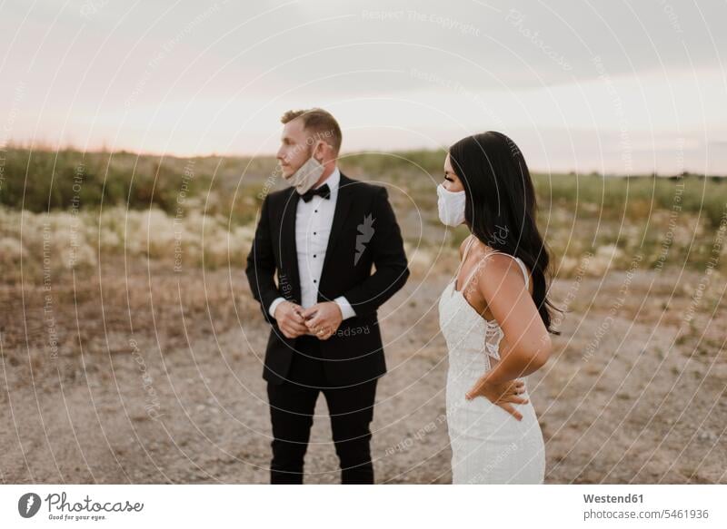 Braut mit Bräutigam trägt eine schützende Gesichtsmaske, während sie während COVID-19 im Feld wegschaut Farbaufnahme Farbe Farbfoto Farbphoto Außenaufnahme