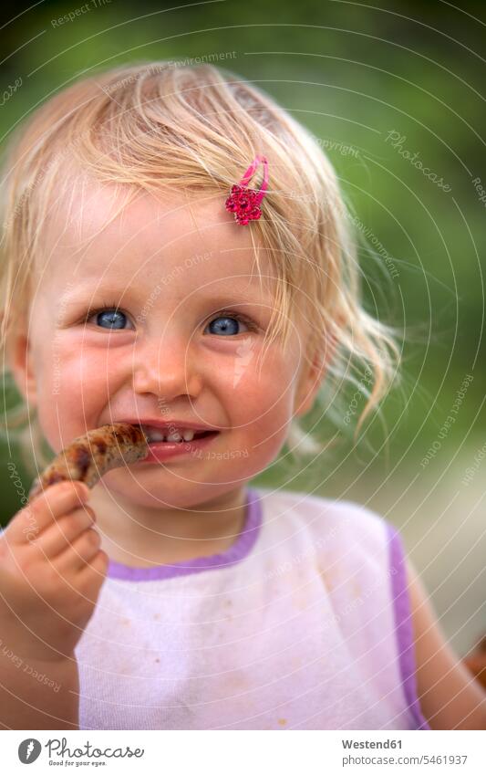 Porträt eines blonden kleinen Mädchens mit Lätzchen und rosa Haipin essen Wurst lächeln Kindheit Würstchen Haarklammer Haarspange Haarnadel Natur Magenta