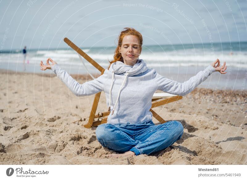 Frau sitzt im Schneidersitz auf Sand und meditiert am Strand Liegestuhl Liegestühle weiblich Frauen Beach Straende Strände Beaches Yoga Yoga-Übungen