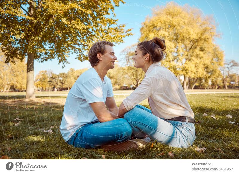 Junges Paar sitzt auf der Wiese in einem Park Wiesen Parkanlagen Parks sitzen sitzend Pärchen Paare Partnerschaft Mensch Menschen Leute People Personen
