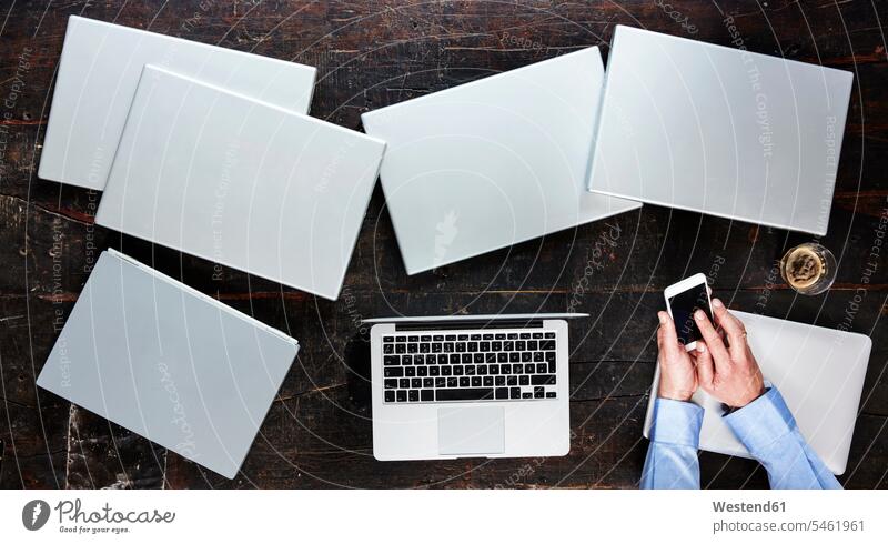 Männerhände mit Smartphone auf einem Tisch mit sieben Laptops, Draufsicht Notebook Notebooks Mann männlich Hand Hände benutzen benützen iPhone Smartphones