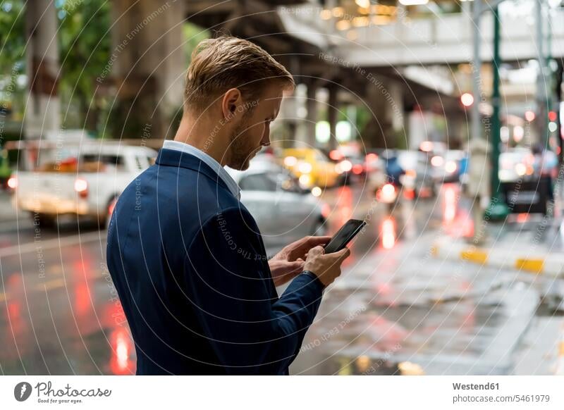 Junger Geschäftsmann benutzt Smartphone in Bangkok an einem regnerischen Tag Leute Menschen People Person Personen Europäisch Kaukasier kaukasisch 1 Ein