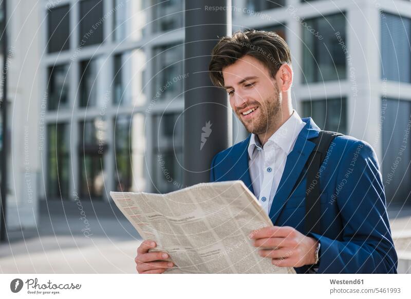Lächelnder Geschäftsmann liest Zeitung in der Stadt lächeln staedtisch städtisch Zeitungen lesen Lektüre Businessmann Businessmänner Geschäftsmänner