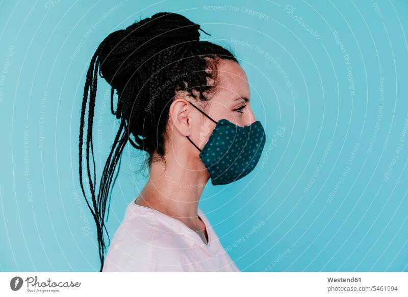 Frau, die eine schützende Gesichtsmaske mit Haarknoten vor türkisfarbenem Hintergrund trägt Farbaufnahme Farbe Farbfoto Farbphoto Spanien Freizeitkleidung