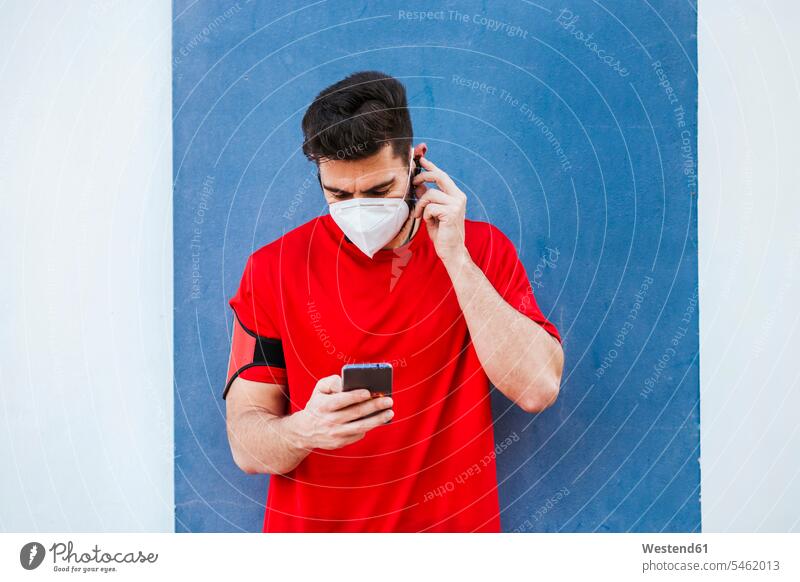 Mittelgroßer, maskierter Mann mit Smartphone, der an der Wand steht Farbaufnahme Farbe Farbfoto Farbphoto Spanien Außenaufnahme außen draußen im Freien Tag