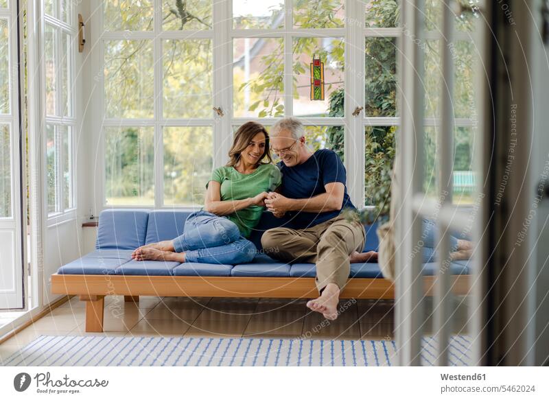Zärtliches reifes Paar sitzt auf Couch zu Hause Couches Liege Sofas daheim sitzend Leute Menschen People Person Personen Paare Partnerschaft Pärchen Europäisch