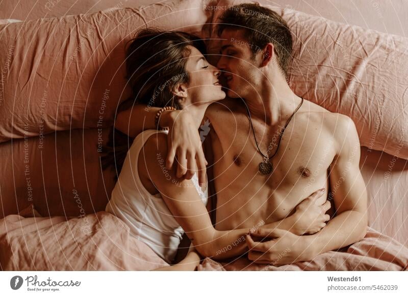 Intimes junges Paar im Bett liegend Betten Schmuckstueck Schmuckstuecke Schmuckstück Schmuckstücke Ketten Halsketten anfassen Berührung knuddeln schmusen Kuss