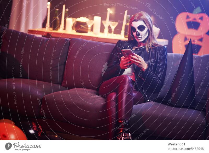 Gelangweilte Frau benutzt Mobiltelefon auf Halloween-Party weiblich Frauen maskiert Parties Partys Smartphone iPhone Smartphones Abend vor Allerheiligen