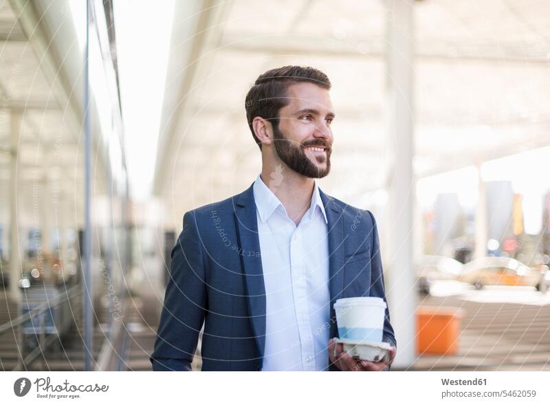 Lächelnder junger Geschäftsmann hält Tablett mit Kaffee zum Mitnehmen Tabletts lächeln Businessmann Businessmänner Geschäftsmänner halten Getränk Getraenk