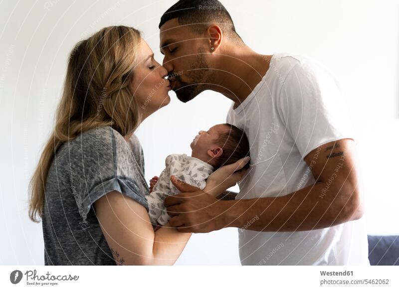 Küssende Eltern halten neugeborenes Baby zu Hause Vater Papas Väter Vati Vatis Papis glücklich Glück glücklich sein glücklichsein Fürsorge kümmern fürsorglich