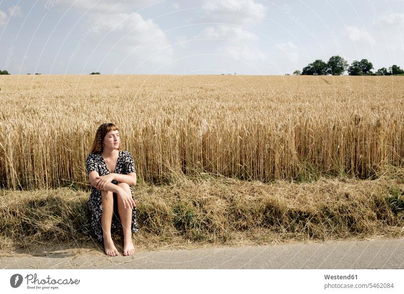 Junge Frau sitzt barfuß am Straßenrand vor einem Getreidefeld Leute Menschen People Person Personen Europäisch Kaukasier kaukasisch erwachsen Erwachsene Frauen