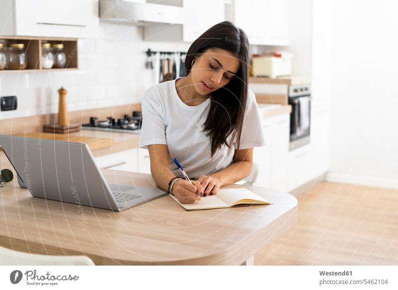 Junge Frau mit Laptop macht Notizen zu Hause Leute Menschen People Person Personen Alleinstehende Alleinstehender Singles Unverheiratete Unverheirateter Job