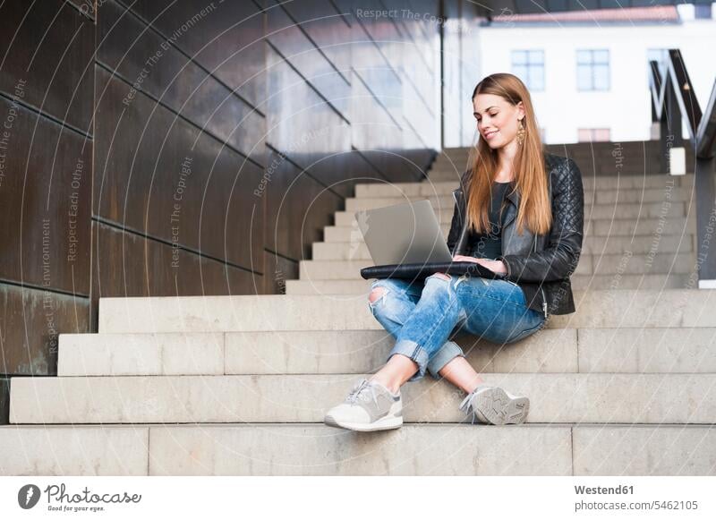 Glückliche junge Frau, die mit einem Laptop auf einer Treppe in einem unterirdischen Gang sitzt Farbaufnahme Farbe Farbfoto Farbphoto Innenaufnahme