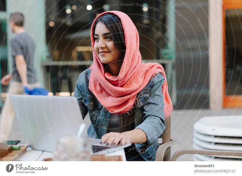 Lächelnde junge Frau mit Laptop und Kopftuch in einem Straßencafé Internet Business Geschäftsleben Geschäftswelt geschäftlich WLan Wireless Lan W-Lan Wifi