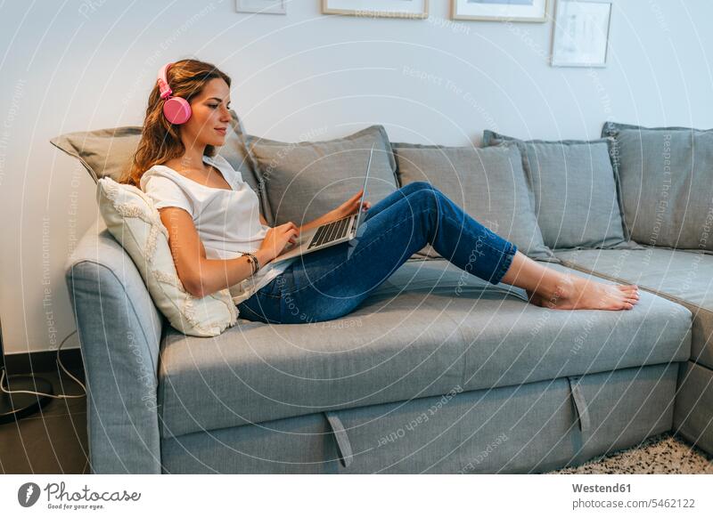 Entspannte junge Frau auf der Couch zu Hause mit Kopfhörer und Laptop Leute Menschen People Person Personen Europäisch Kaukasier kaukasisch 1 Ein ein Mensch
