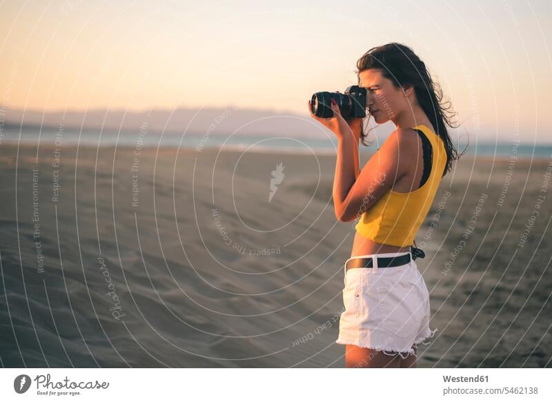 Teenager-Mädchen fotografiert mit Kamera am Strand bei Sonnenuntergang Foto Fotos Sonnenuntergänge Beach Straende Strände Beaches Teenagerin junges Mädchen