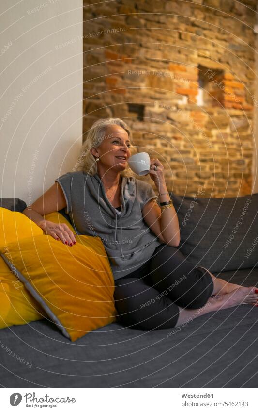 Glückliche reife Frau entspannt auf Couch mit Tasse Kaffee Italien Naturstein Natursteine ausruhen Rast Erholung erholen Lichtschein Best Ager bestes Alter