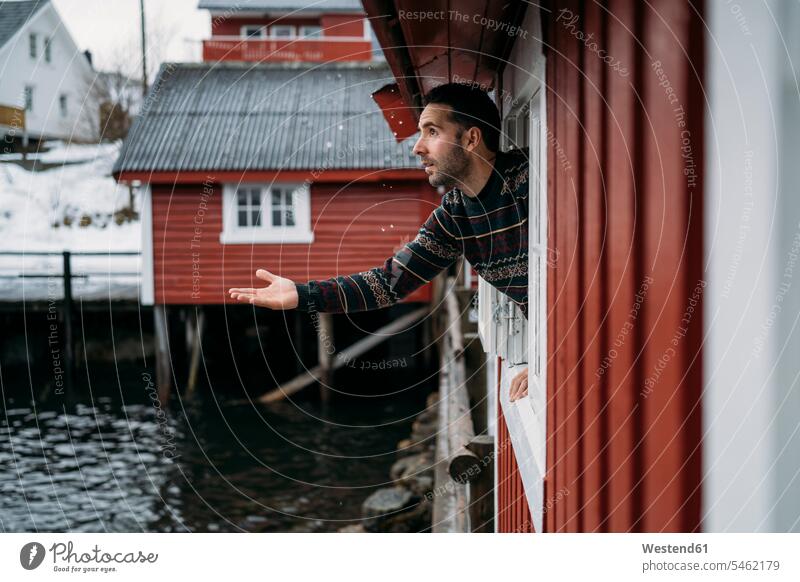 Tourist, der sich aus dem Fenster einer Hütte lehnt, Lofoten, Norwegen Touristen Jahreszeiten winterlich Winterzeit Muße testen ueberpruefen überprüfen Travel
