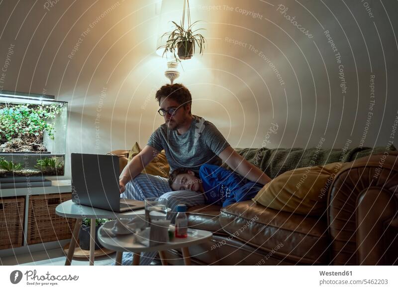 Mann konsultiert Arzt über Laptop, während er bei seiner kranken Tochter sitzt, die zu Hause auf dem Sofa schläft Farbaufnahme Farbe Farbfoto Farbphoto