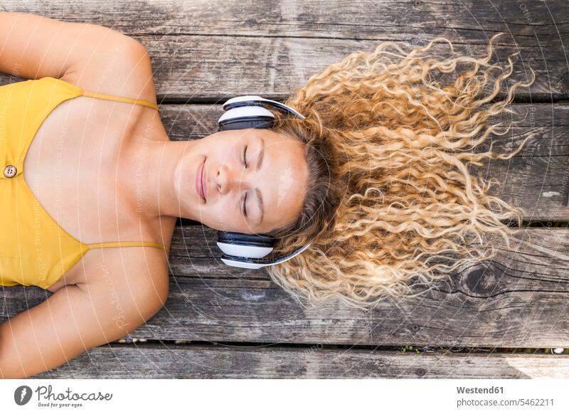 Lächelnde Frau beim Musikhören, auf Holz liegend Kopfhoerer entspannen relaxen hoeren entspanntheit relaxt freuen geniessen Genuss Glück glücklich sein