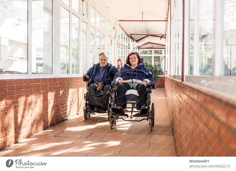 Behinderter Mann und Frau im Rollstuhl im Korridor Farbaufnahme Farbe Farbfoto Farbphoto Innenaufnahme Innenaufnahmen innen drinnen Tag Tageslichtaufnahme