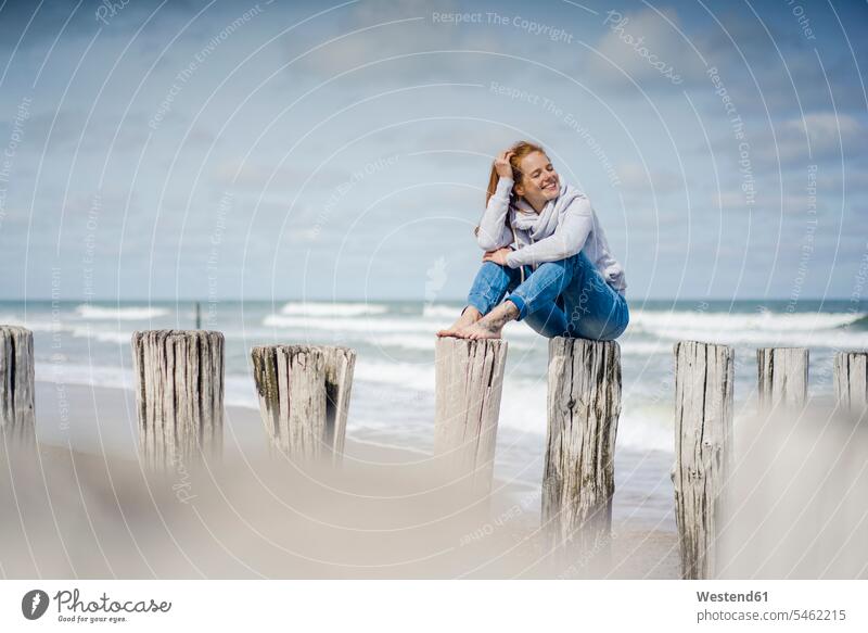 Frau sitzt auf einem Zaun am Strand und entspannt sich am Meer Zäune Beach Straende Strände Beaches weiblich Frauen Entspannung Entspannen relaxen entspannen
