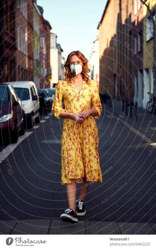 Rothaarige Frau trägt eine FFP2-Gesichtsmaske und geht auf leerer Straße gelbe gelber gelbes Leute Menschen People Person Personen Europäisch Kaukasier