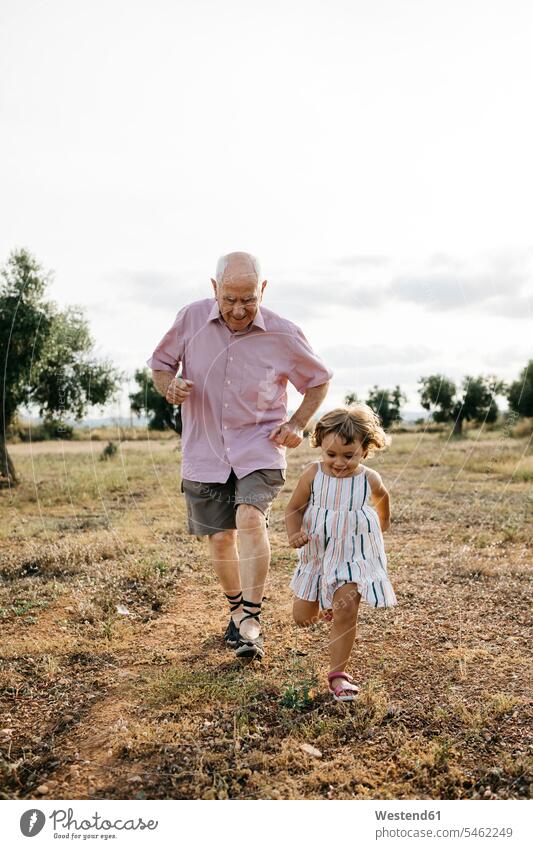 Verspielter Grossvater mit Enkelin, die an Land gegen den Himmel rennen Farbaufnahme Farbe Farbfoto Farbphoto Spanien Freizeitbeschäftigung Muße Zeit Zeit haben