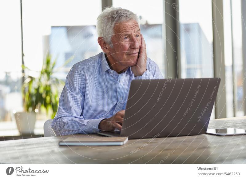 Porträt eines nachdenklichen älteren Mannes, der am Tisch mit Laptop sitzt und in die Ferne schaut schauen schauend anschauen betrachten Portrait Porträts