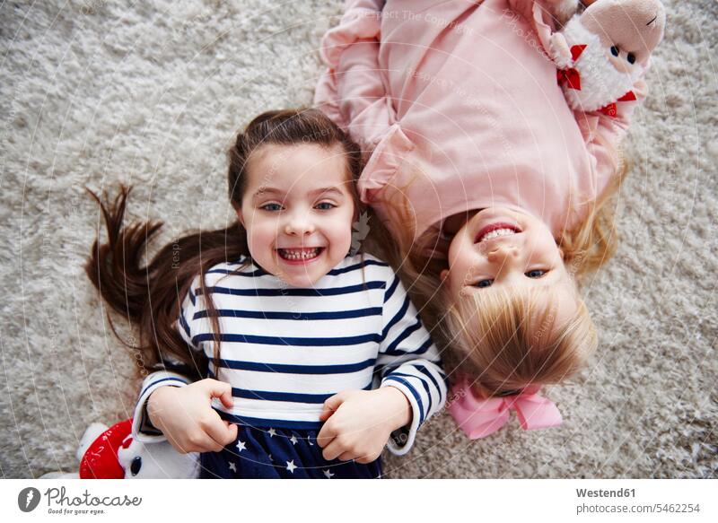 Porträt von zwei grinsenden kleinen Schwestern, die auf dem Teppich liegen Portrait Porträts Portraits Teppiche liegend liegt Europäerin Europäerinnen