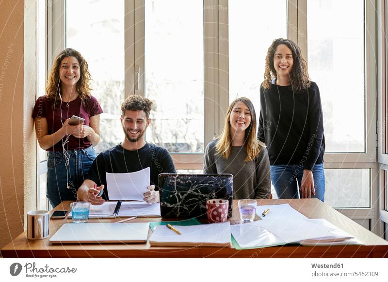 Porträt von vier glücklichen Studenten am Schreibtisch und am Fenster lernen Gemeinsam Zusammen Miteinander Hochschueler Studierender Hochschüler Arbeitstisch