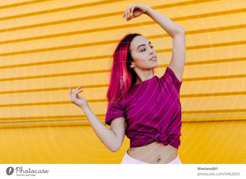 Junge Frau mit gefärbten Haaren schaut weg, während sie gegen die gelbe Wand tanzt Farbaufnahme Farbe Farbfoto Farbphoto Spanien Freizeitbeschäftigung Muße Zeit