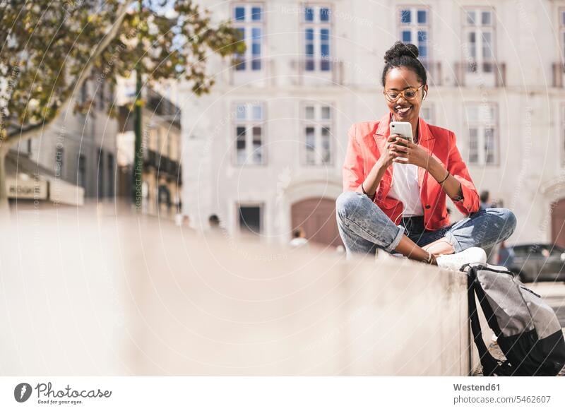 Lächelnde junge Frau mit Kopfhörern und Smartphone in der Stadt, Lissabon, Portugal geschäftlich Geschäftsleben Geschäftswelt Geschäftsperson Geschäftspersonen