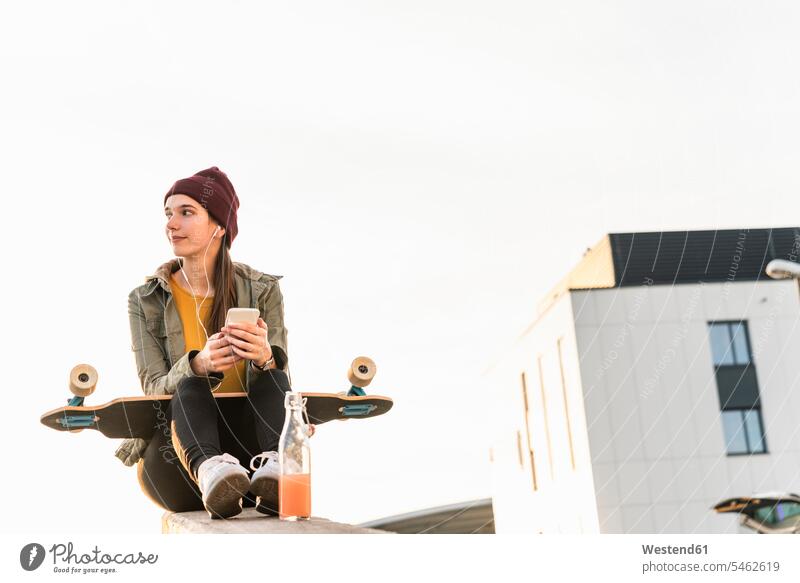 Stilvolle junge Frau mit Skateboard und Handy sitzt auf einer Mauer Leute Menschen People Person Personen Europäisch Kaukasier kaukasisch 1 Ein ein Mensch