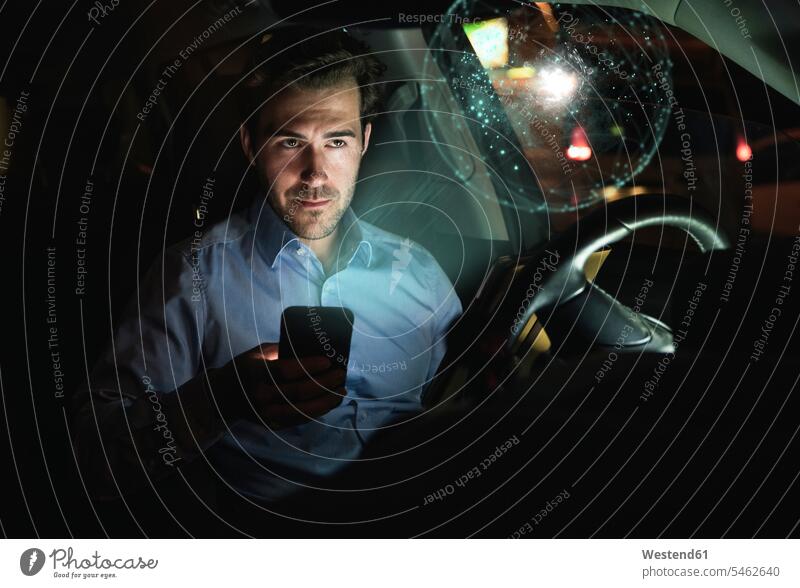 Geschäftsmann nutzt Smartphone nachts im Auto, umgeben von einem virtuellen leuchtenden Globus Leute Menschen People Person Personen Kraftfahrer Job Berufe