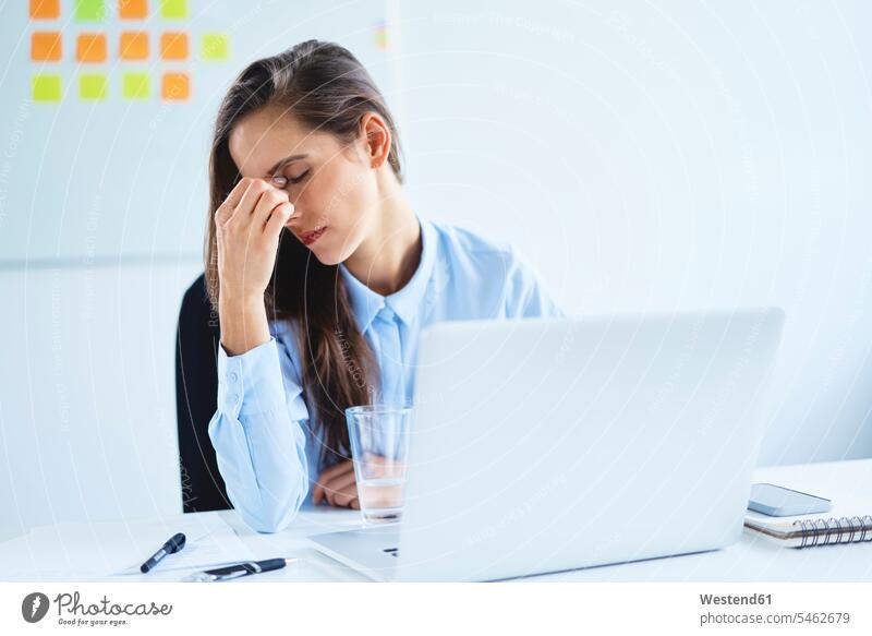 Junge Frau sitzt mit Kopfschmerzen im Büro Job Berufe Berufstätigkeit Beschäftigung Jobs geschäftlich Geschäftsleben Geschäftswelt Geschäftsperson