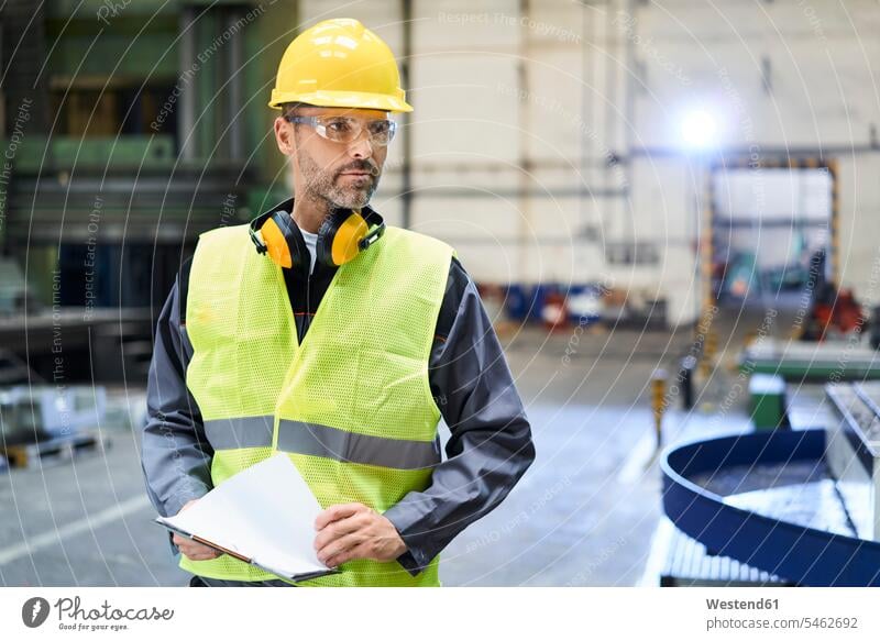 Mann in Arbeitsschutzkleidung schaut sich in der Fabrik um Schutzkleidung Fabrikgebäude Fabrikgebaeude Fabriken Männer männlich umherblicken umschauen umsehen