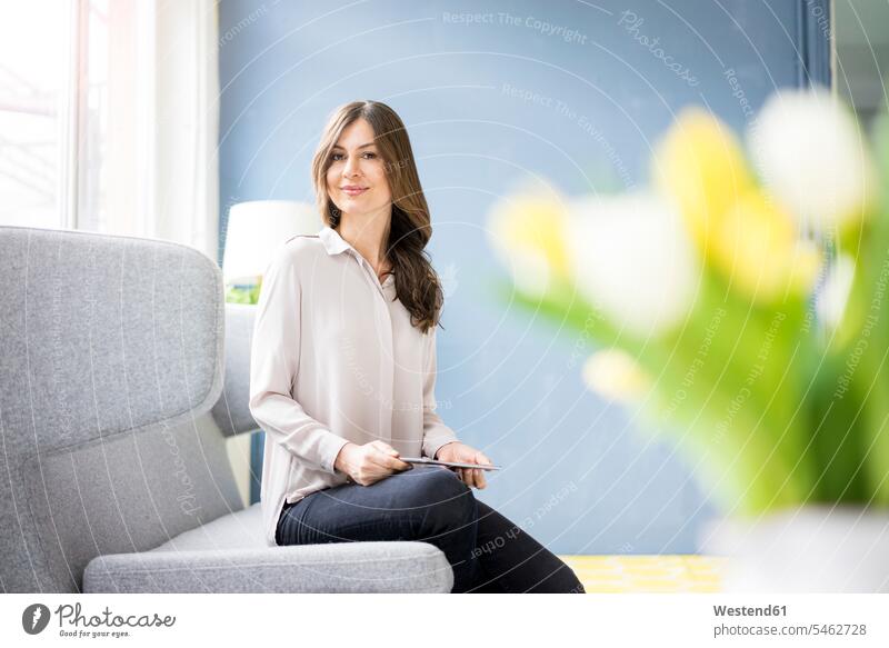 Porträt einer lächelnden Frau, die auf einer Couch sitzt und ein Tablett hält Portrait Porträts Portraits halten weiblich Frauen sitzen sitzend Tablet Computer