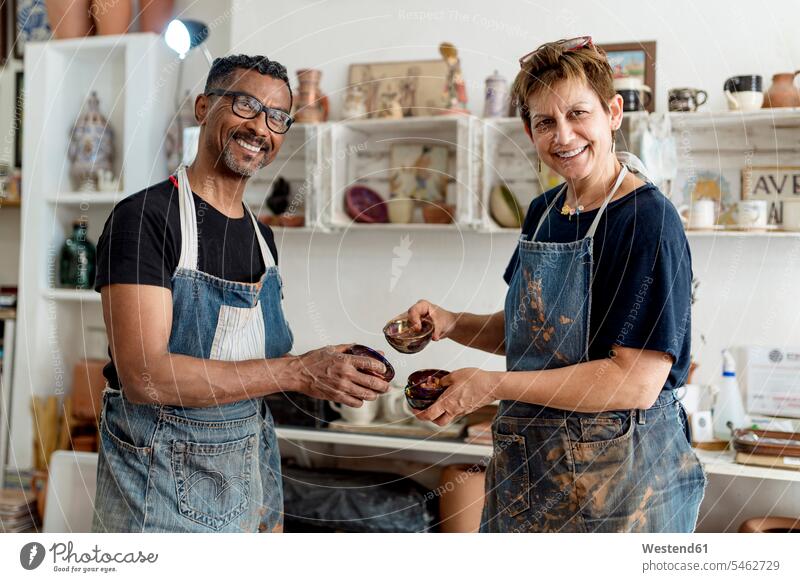 Lächelnde Mitarbeiter, die Keramiken halten, während sie in der Werkstatt stehen Farbaufnahme Farbe Farbfoto Farbphoto Spanien Innenaufnahme Innenaufnahmen