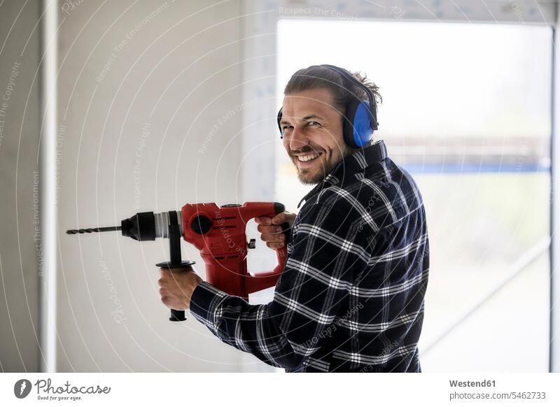 Porträt eines lächelnden Arbeiters, der eine elektrische Bohrmaschine auf einer Baustelle benutzt Job Berufe Berufstätigkeit Beschäftigung Jobs freuen Frohsinn