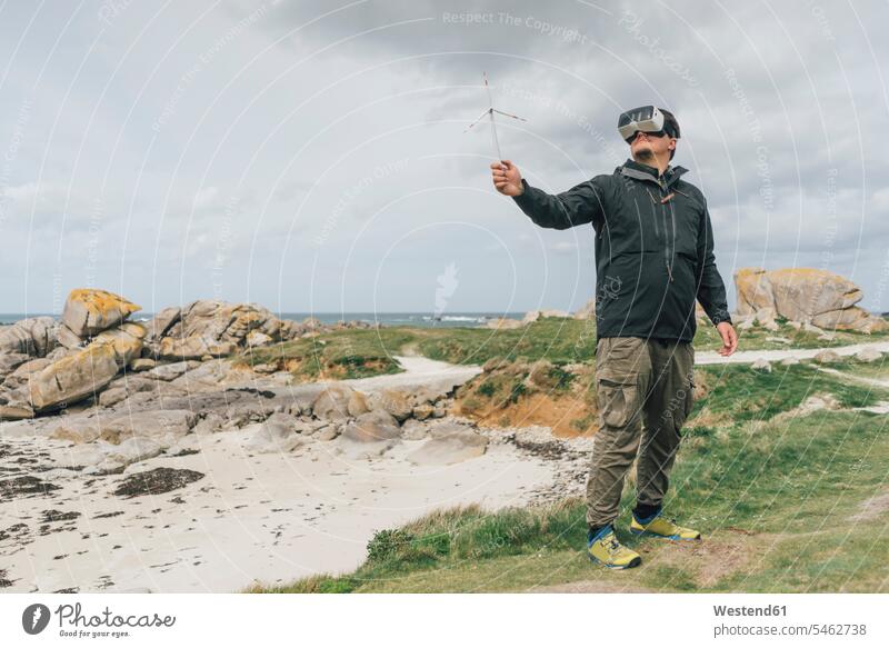 Frankreich, Bretagne, Meneham, Mann mit Miniatur-Windturbine mit VR-Brille an der Küste Miniaturen Windrad Brillen Küstenlandschaft Männer männlich virtuell