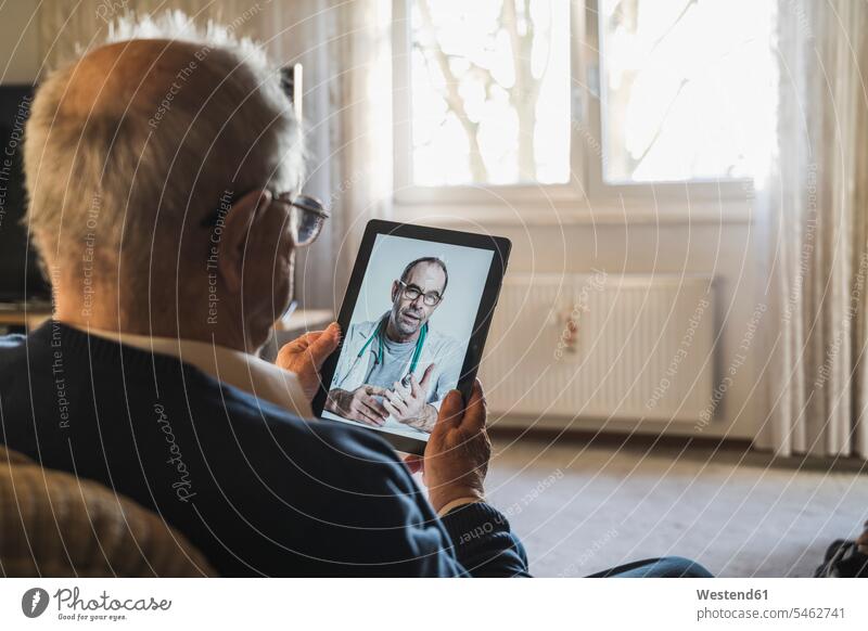 Älterer Mann, der sich von einem männlichen Arzt per Videoanruf über ein digitales Tablet zu Hause beraten lässt Farbaufnahme Farbe Farbfoto Farbphoto