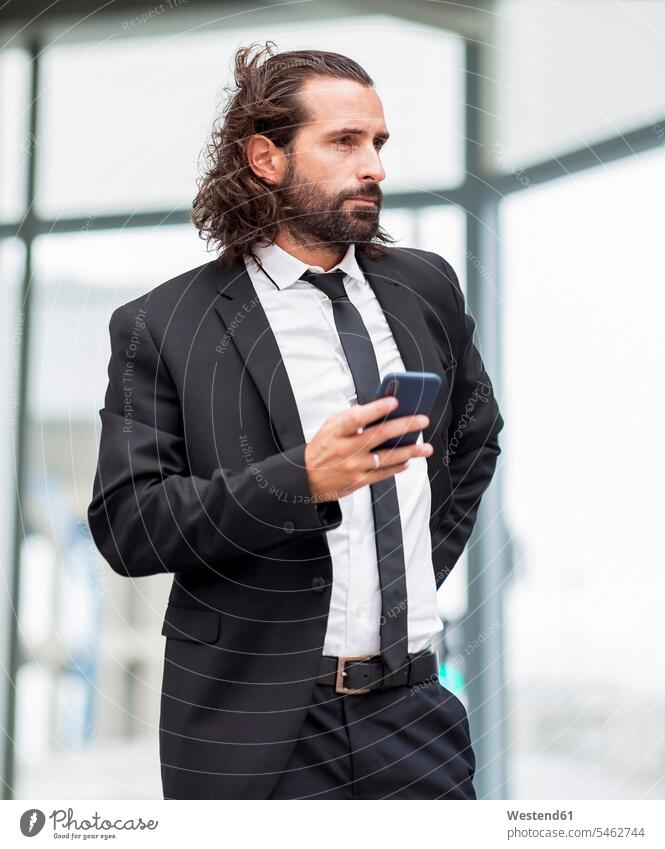 Porträt eines bärtigen Geschäftsmannes, der mit einem Smartphone in der Hand drinnen steht Innenaufnahme Innenaufnahmen Tag Tageslichtaufnahme