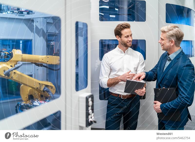 Zwei Geschäftsleute unterhalten sich an einem Roboter in einer modernen Fabrik Arbeitskollege Arbeitskollegen Kollege Partner Partnerschaften Job Berufe