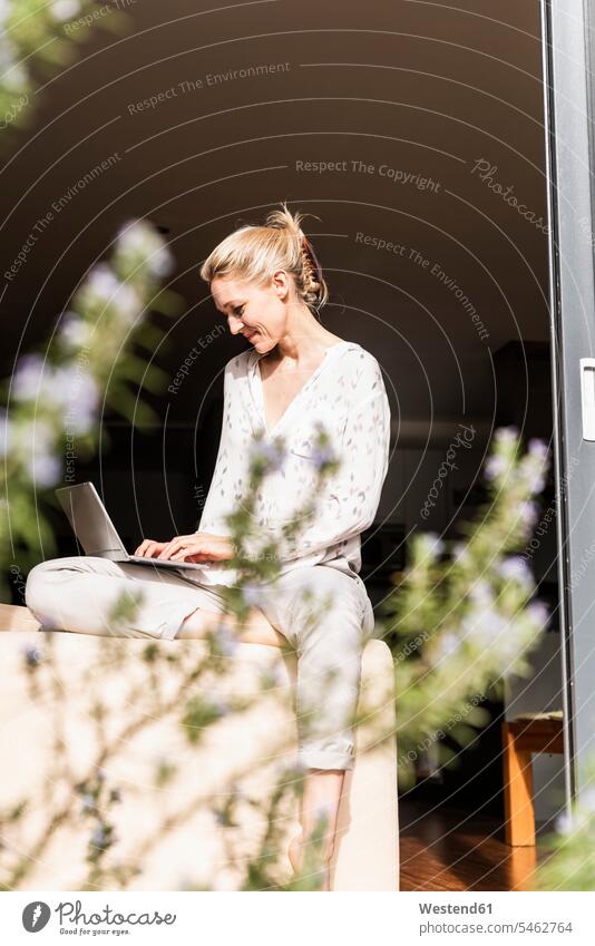Lächelnde reife Frau sitzt mit Laptop an offener Terrassentür Notebook Laptops Notebooks lächeln sitzen sitzend weiblich Frauen benutzen benützen Computer