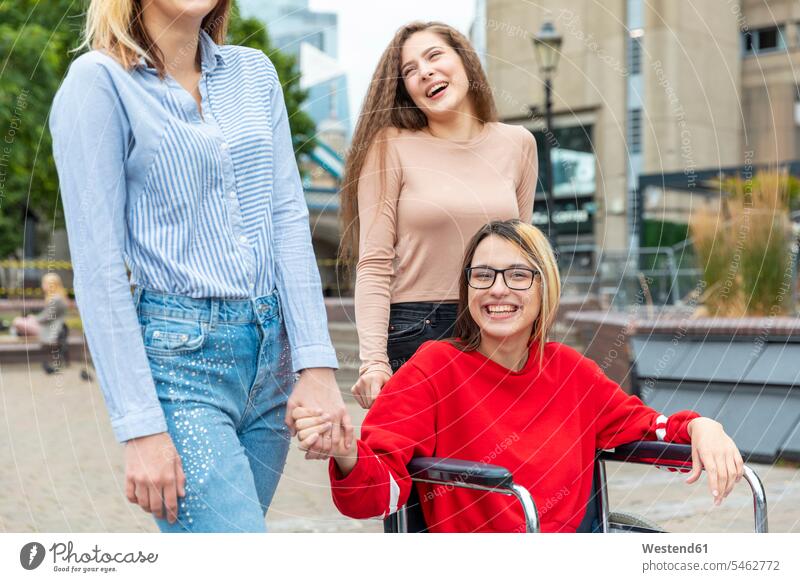 Glückliche behinderte Frau im Rollstuhl verbringt ihre Freizeit mit Freundinnen in der Stadt Farbaufnahme Farbe Farbfoto Farbphoto Außenaufnahme außen draußen